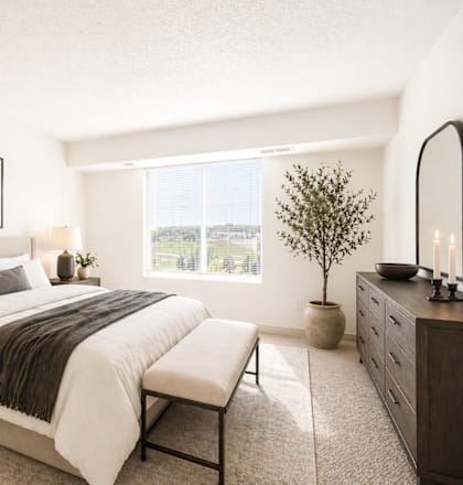 A well-lit bedroom with a large bed, a side table with a lamp, and a framed picture on the wall.