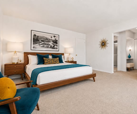 A bedroom with a bed, two nightstands, a chair, and a framed picture on the wall.