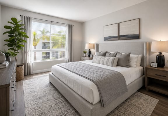 A bedroom with a large bed, a nightstand, and a window with blinds.