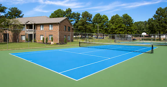 A tennis court is surrounded by a fence and a brick building.