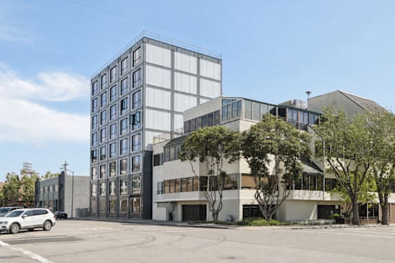 A modern building with a glass facade stands next to a smaller structure with a white exterior.
