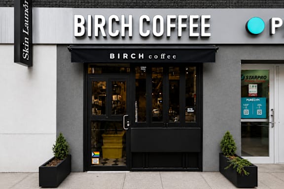 A storefront of Birch Coffee with a black awning and a green sign on the door.