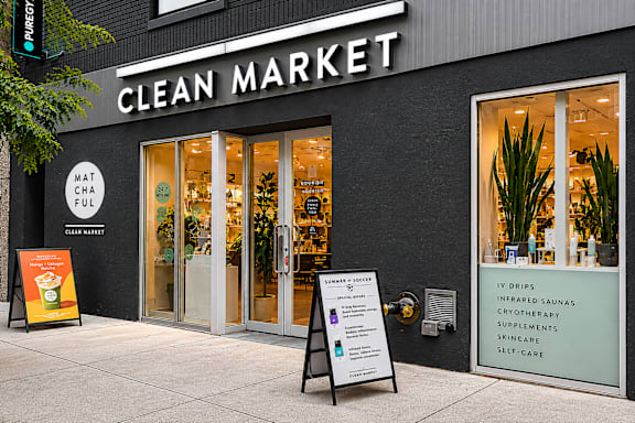 A storefront of a Clean Market with a signboard and a small tree.