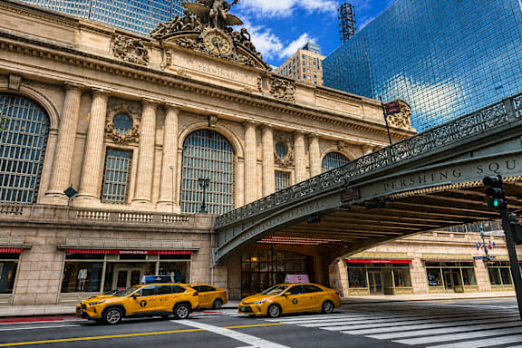 A yellow taxi is driving past a building with a sign that reads "Pershing Square.".