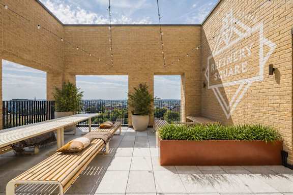 A patio with a table and chairs is under a sign that says "Refinery Squares.".