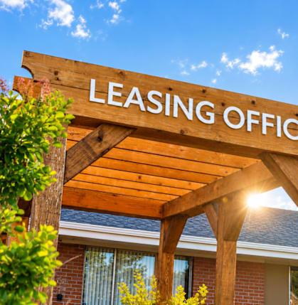 A wooden leasing office sign is displayed in front of a building.