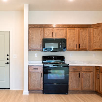 A kitchen with a black fridge and microwave, wooden cabinets, and a white door.
