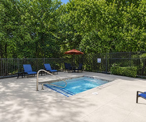 A pool surrounded by trees and chairs.