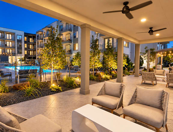 A patio with chairs and a table is illuminated by lights.