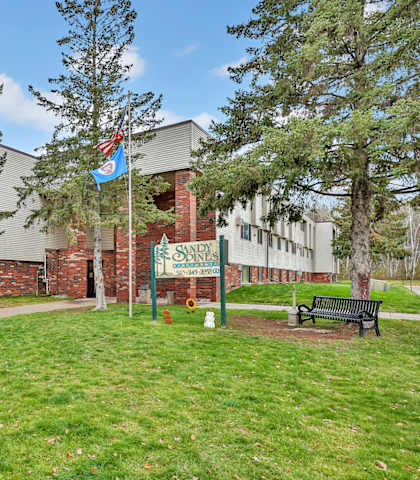 the front of a school building with a green lawn and a bench