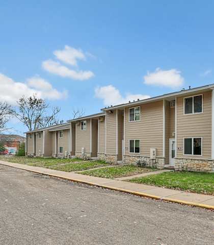 A row of houses with a sidewalk and a tree in the distance.