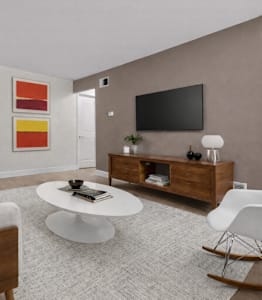 A modern living room with a white sofa, a white coffee table, a white rocking chair, a wooden cabinet, a flat screen TV, and a painting on the wall.