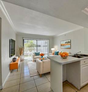 A kitchen with white cabinets and appliances, a dining table with chairs, and a living room with a couch and a TV.