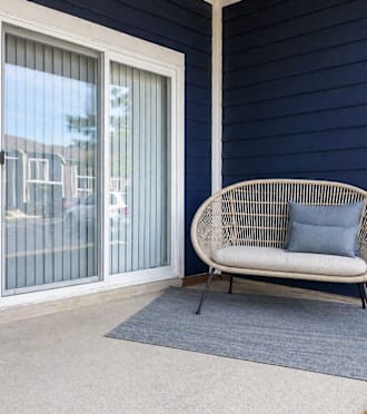 A white chair with a blue cushion is placed on a blue rug in front of a glass door.