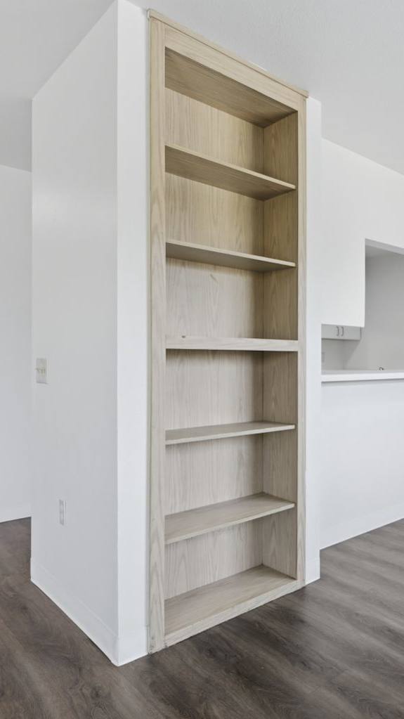 A room with a white wall and a wooden floor with a shelving unit.