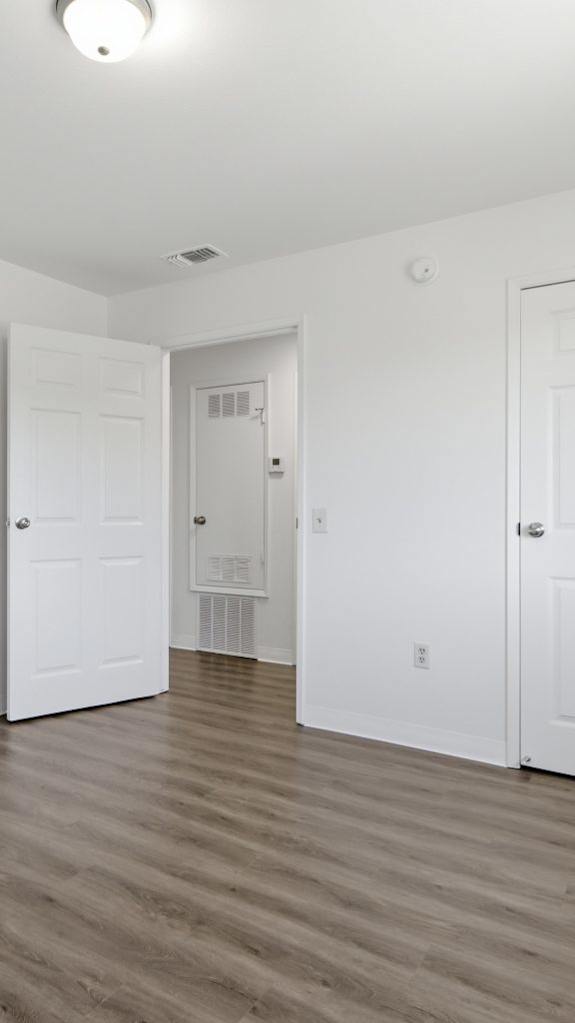 A room with white walls and wooden flooring with three doors.