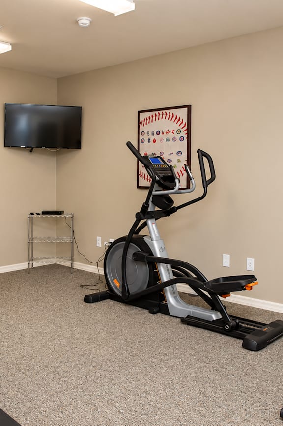 A room with a treadmill, exercise bike and a television.