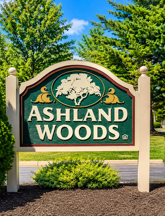 A sign for Ashland Woods is displayed in front of some trees.