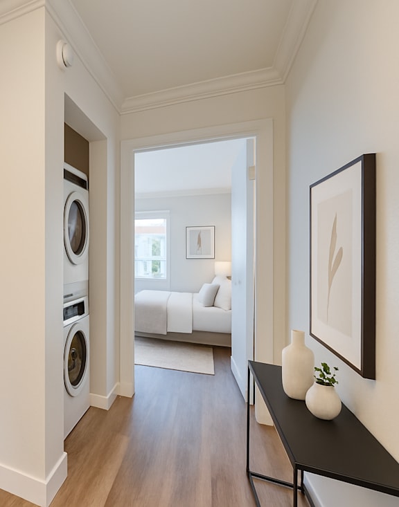 A kitchen with white cabinets and a washer and dryer in the hallway.
