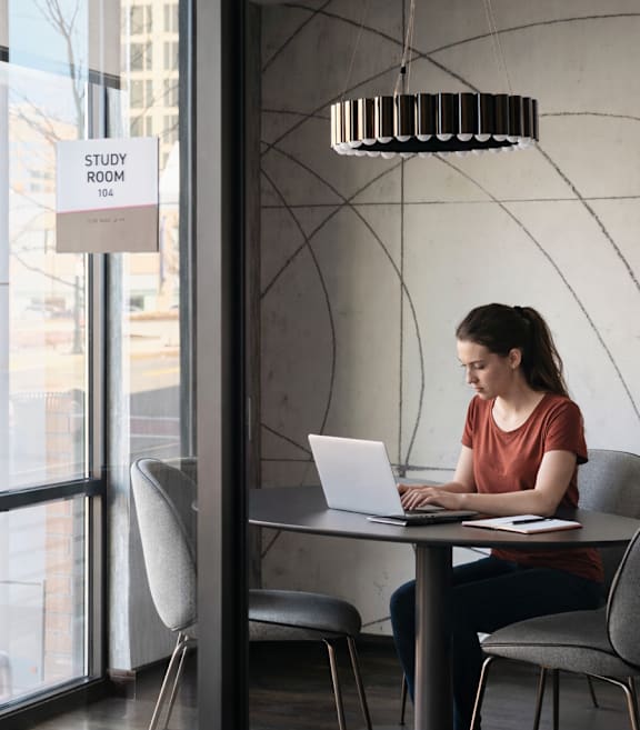 A woman is sitting at a table in a study room with a laptop.