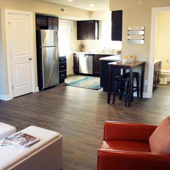 A room with a wooden floor and a kitchenette in the background.