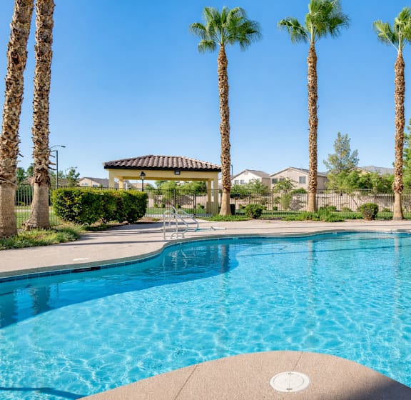 A swimming pool surrounded by palm trees and a gazebo.