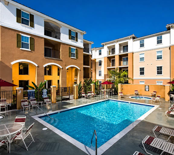 A swimming pool surrounded by chairs and umbrellas in front of a building.