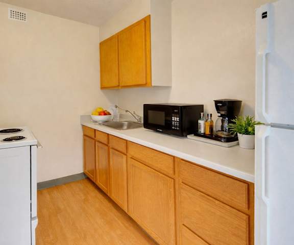 A cozy kitchen with white appliances, light counter with ample space, and spacious wooden cabinets at Mendenhall Tower Apartments. 