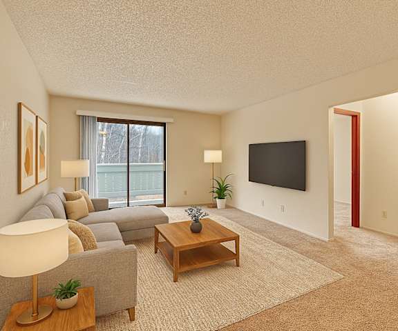 A large empty living room with carpeting, a plant in the corner, and a door to the balcony at Park Plaza Apartments. 