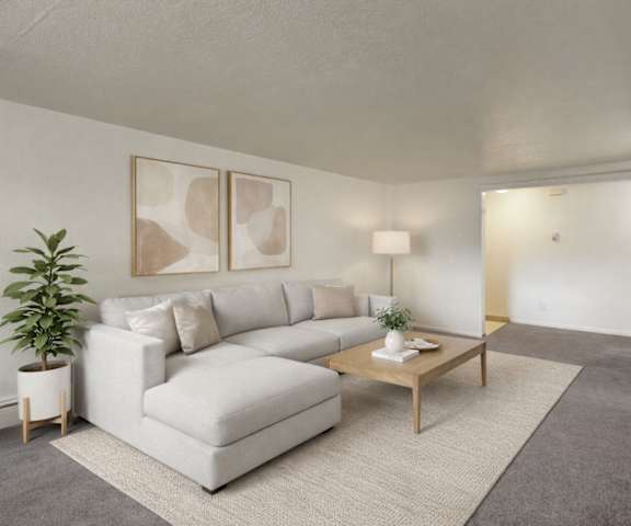 A view of the empty carpeted living room with a door to the balcony and the kitchen with white appliances and wooden large cabinets at Ptarmigan Meadows Apartment Homes