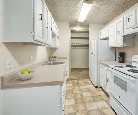 A cozy kitchen with white appliances, a red counter with lots of room, and spacious white wooden cabinets at Quiet Creek Apartments. 