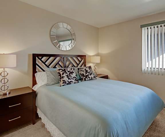 A bedroom with a bed and a window with vertical blinds at Alpine Apartments. 