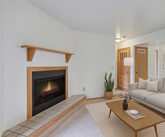 An empty living room with carpeting, fireplace, overhead lighting, a door to the patio at Wildwood Estates Apartment Homes. 