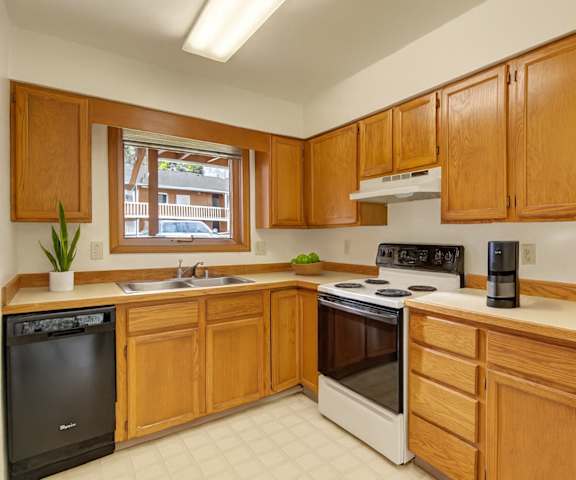 A cozy kitchen with white appliances, light counter, and large wooden cabinets at Wildwood Estates Apartment Homes. 