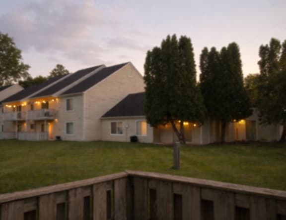 A house with a white exterior and a black roof is surrounded by trees and has lights on.