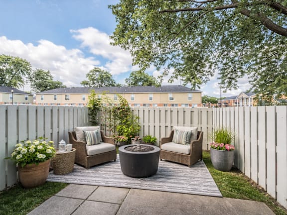 A white fence encloses a cozy outdoor seating area with a couch, chairs, and potted plants.