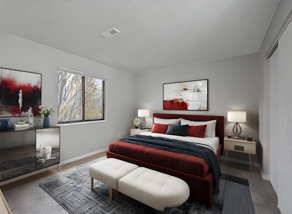 A bedroom with a red bedspread and a large painting on the wall.
