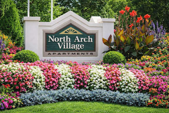 A sign for North Arch Village Apartments is surrounded by a flower bed.