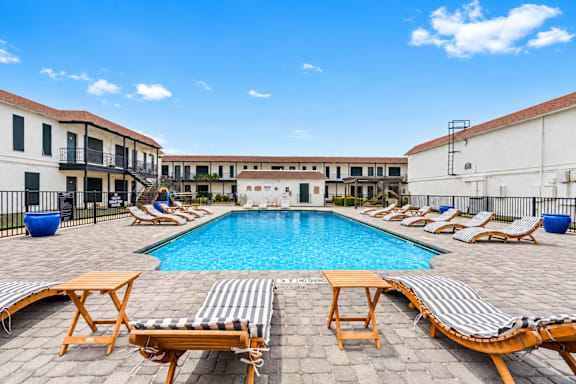 A pool surrounded by lounge chairs and tables.