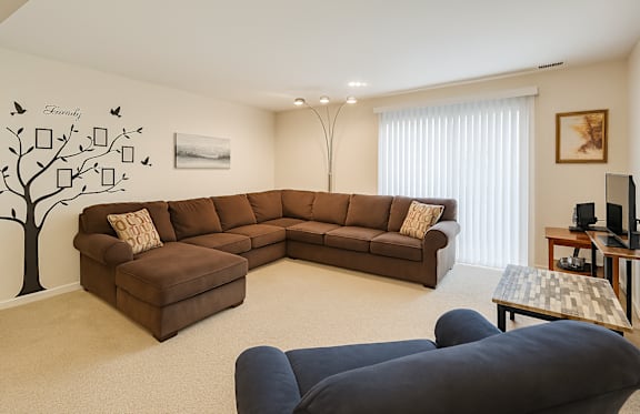 A living room with a brown sectional sofa and a tree mural on the wall.