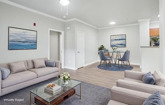 A living room with a grey couch, a glass coffee table, and a painting of a beach scene on the wall.