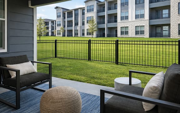 A patio with a black chair, a brown ottoman, and a black railing.