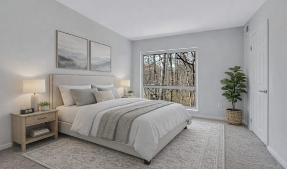 A bedroom with a large bed, a nightstand with a lamp, and a window with a view of trees.