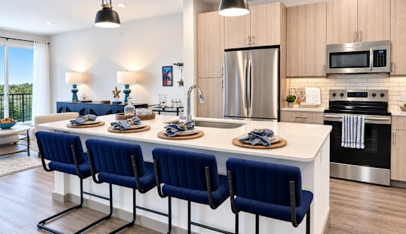 A kitchen with a long white island and blue chairs.