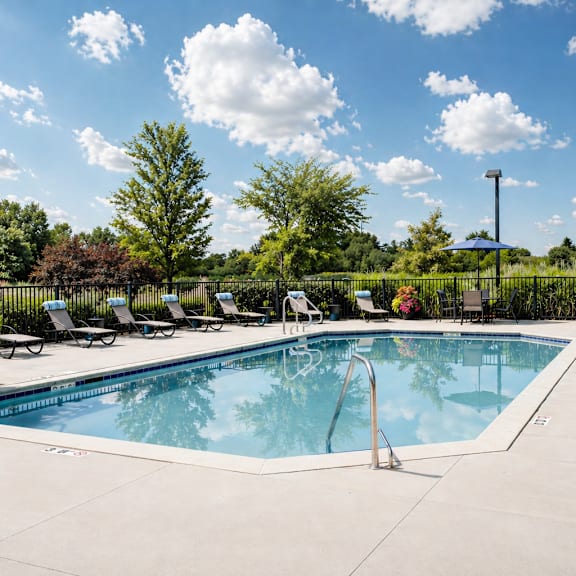 A large outdoor swimming pool surrounded by lounge chairs and trees.