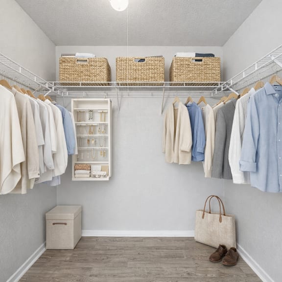 A white closet with clothes hanging and a brown bag on the floor.