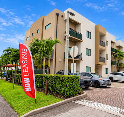 A building with a red sign that says "NOW LEASING" in front of it.