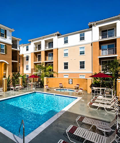 A swimming pool surrounded by chairs and umbrellas in front of a building.