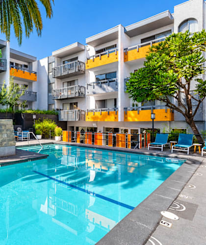 A swimming pool in front of a building with palm trees.