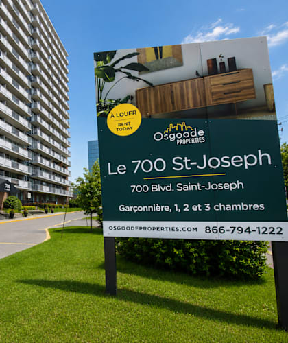 A sign for Le 700 St-Joseph is in front of a tall apartment building.